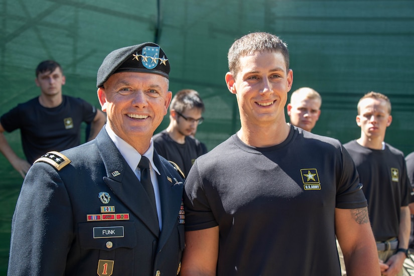 Older Army Soldier in uniform poses with young, smiling teenage male.