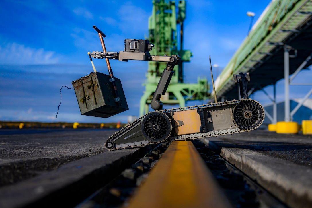 A robotic vehicle balances on a pier as it carries a heavy  package.