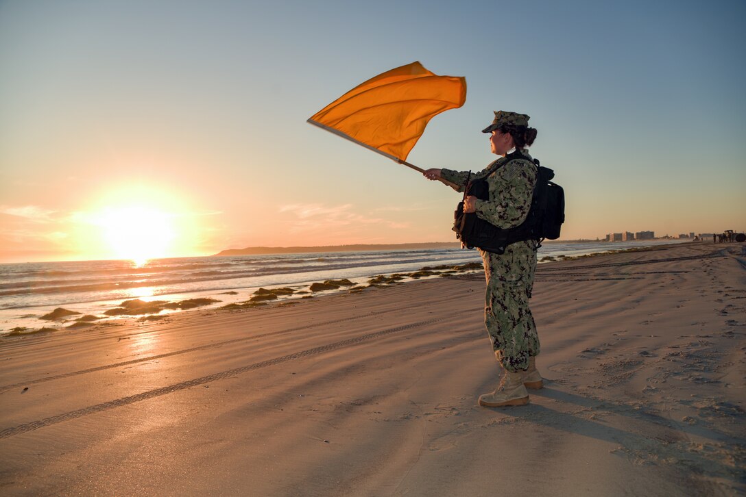 A sailor waves a yellow flag on a beach.