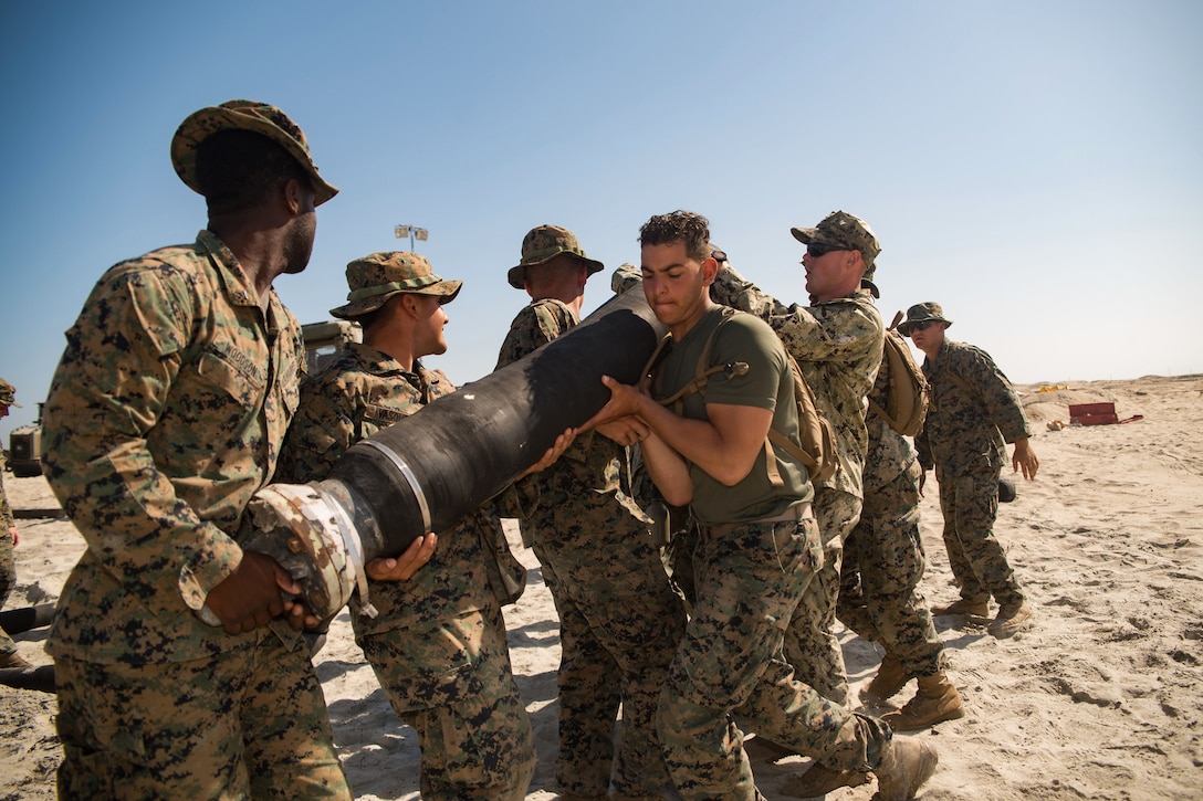 A group of Marines on a beach carry a large hose.