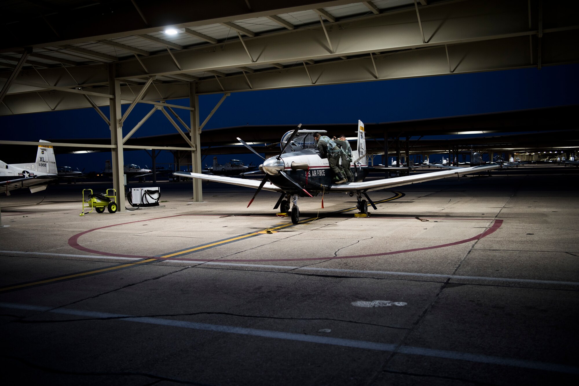 First Lt. Benjamin Peña and 1st Lt. Nicholas Myers, 85th Flying Training Squadron instructor pilots, place items inside a T-6A Texan II before takeoff on Sept. 18, 2019 at Laughlin Air Force Base, Texas. Night flying at a Specialized Undergraduate Pilot Training base allows not only more hours in the sky, but it also provides a variety experience so pilots can become accustomed to instrument flying. (U.S. Air Force photo by Senior Airman Marco A. Gomez)