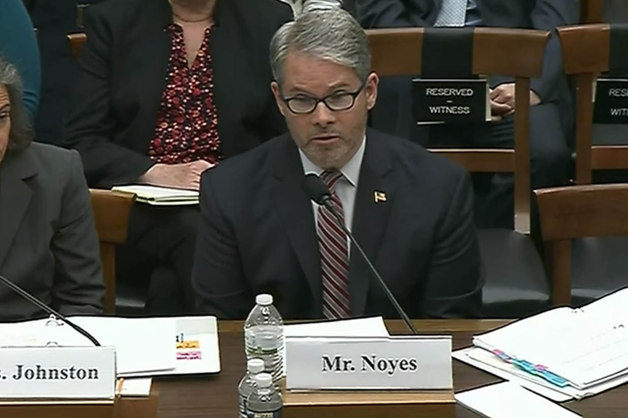 Man in suit sits in front of a microphone at a hearing.