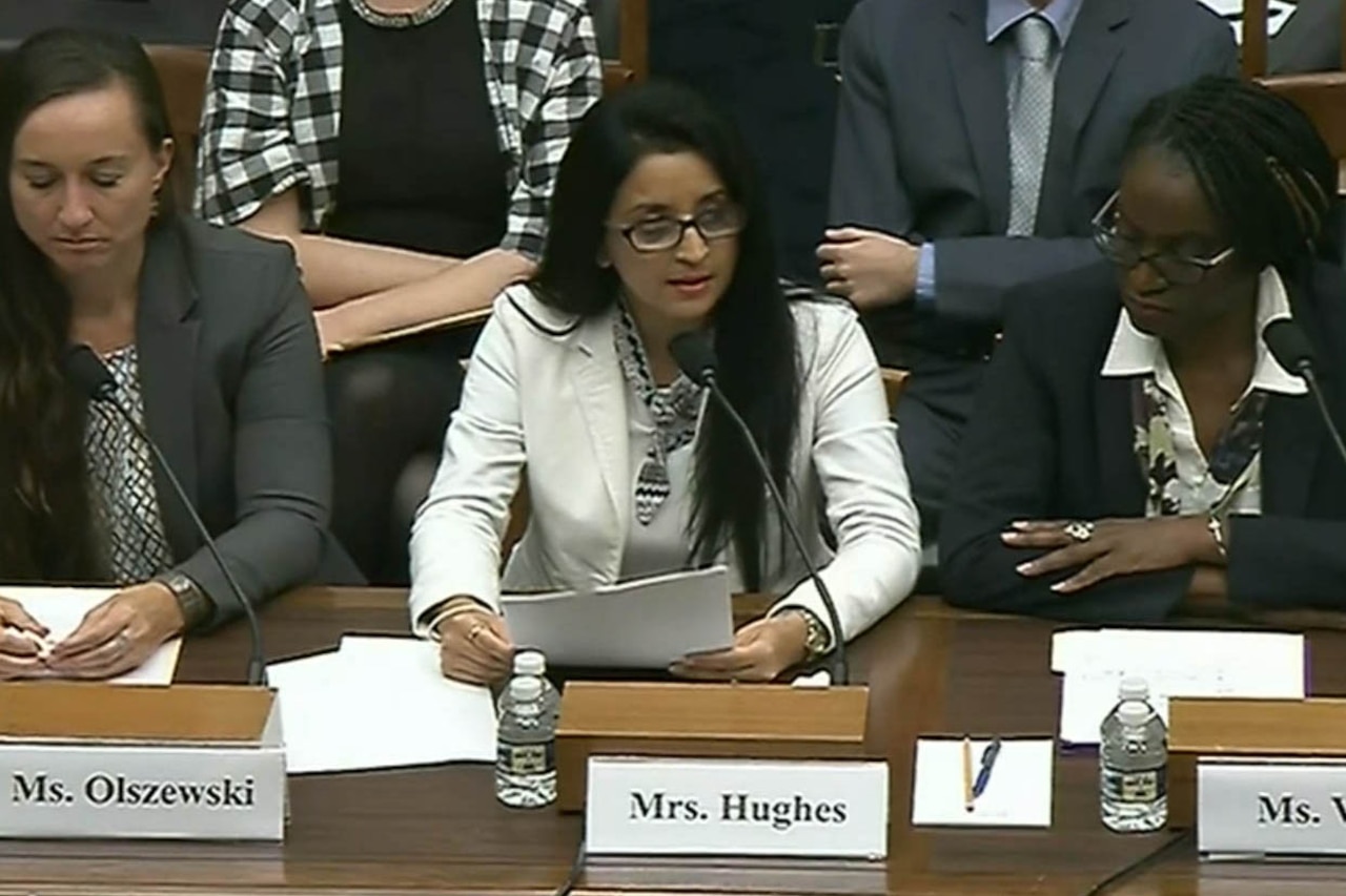 Three women sit at a table behind microphones in preparation to speak at a hearing.