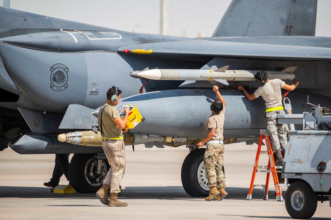 Three airmen load munitions onto an aircraft.