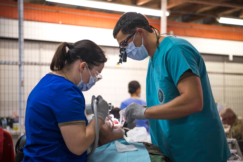 Two dental professionals do work on a patient in a chair.