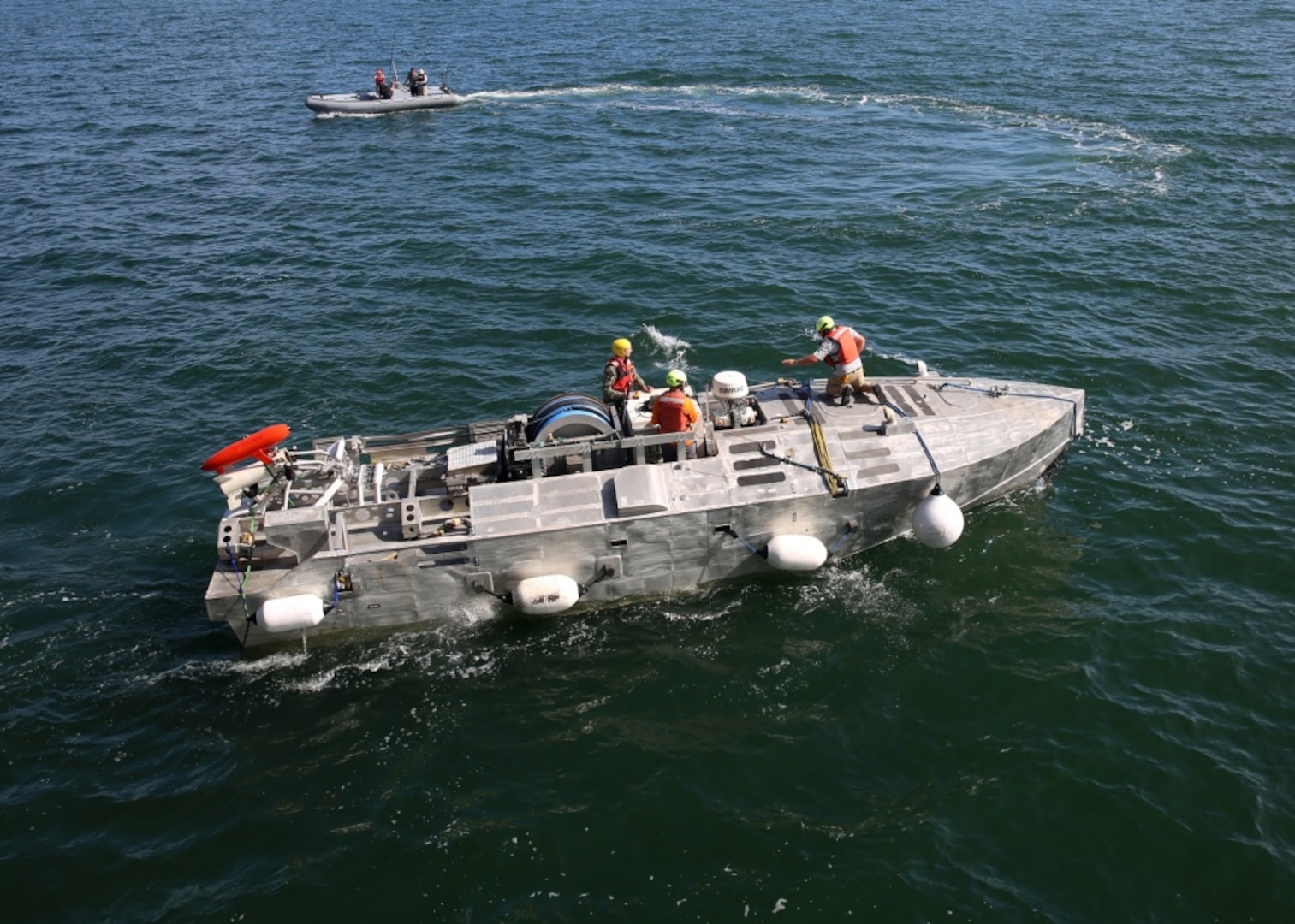 A Sailor and civilian technicians monitor an unmanned surface vehicle (USV)