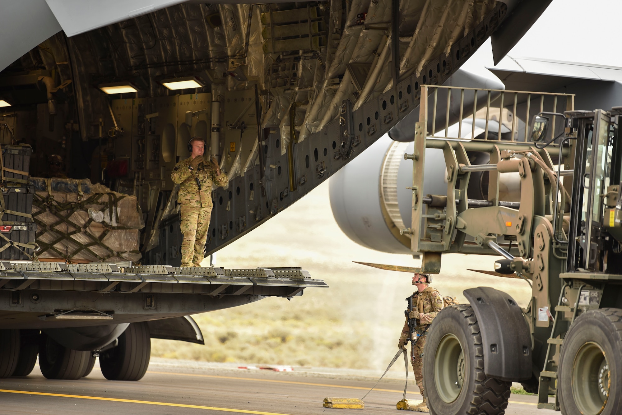 A U.S. Air Force Airman directs a forklift towards a C-17 Globemaster III to unload cargo from the C-17 as part of a Joint Forcible Entry operation during Air Mobility Command’s Mobility Guardian exercise.