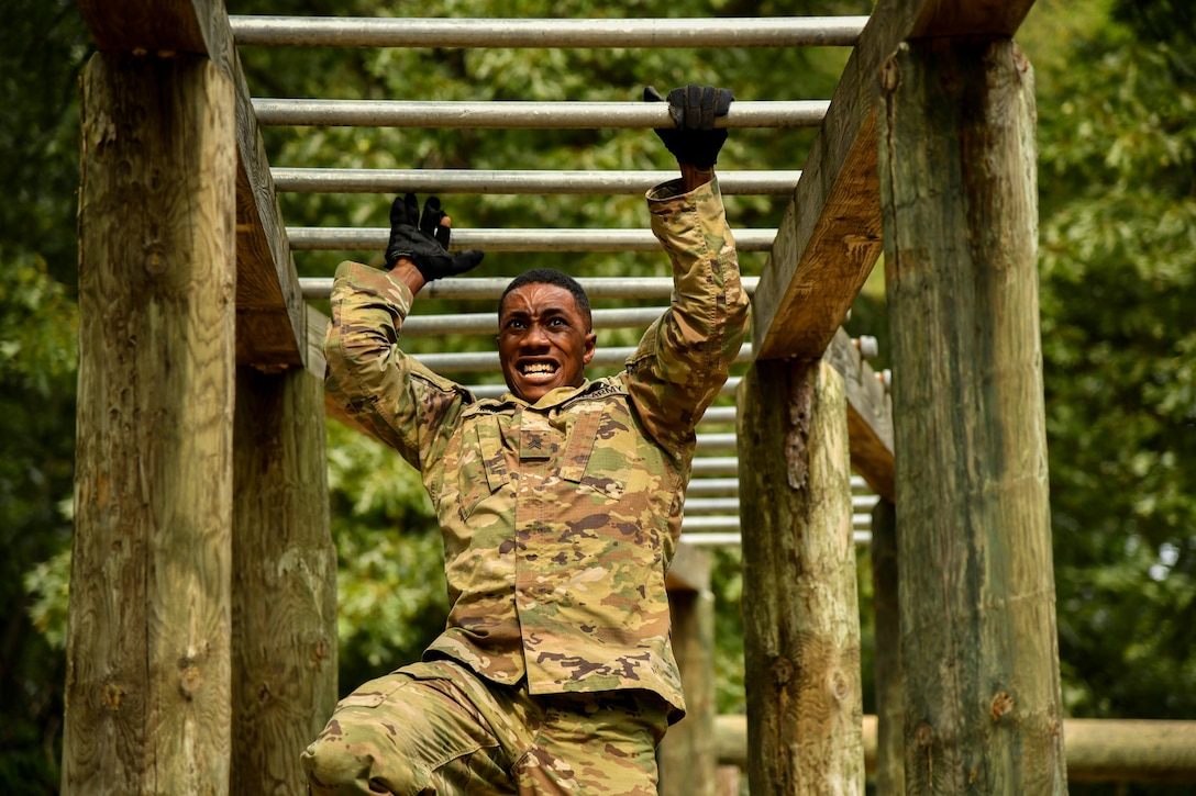 A soldier swings from one bar to the next on an obstacle.