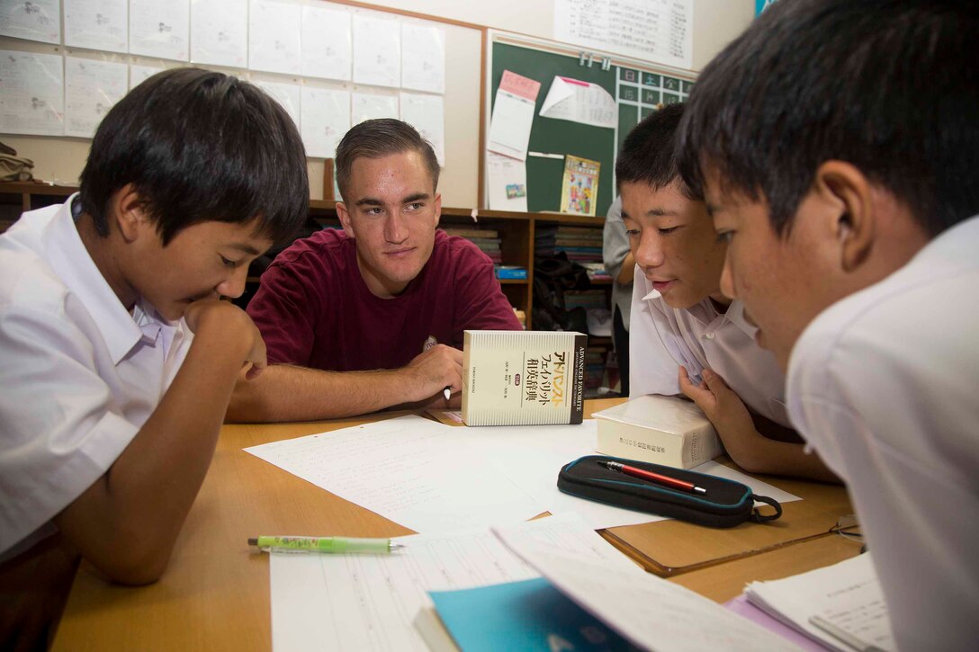 リンチ上等兵が中学生が読む英文を聞き確認しています。伊江島補助飛行場の海兵隊員らが今年２月から、伊江村立伊江中学校を週に一度訪れ、英語の授業で生徒たちのサポートをしています。