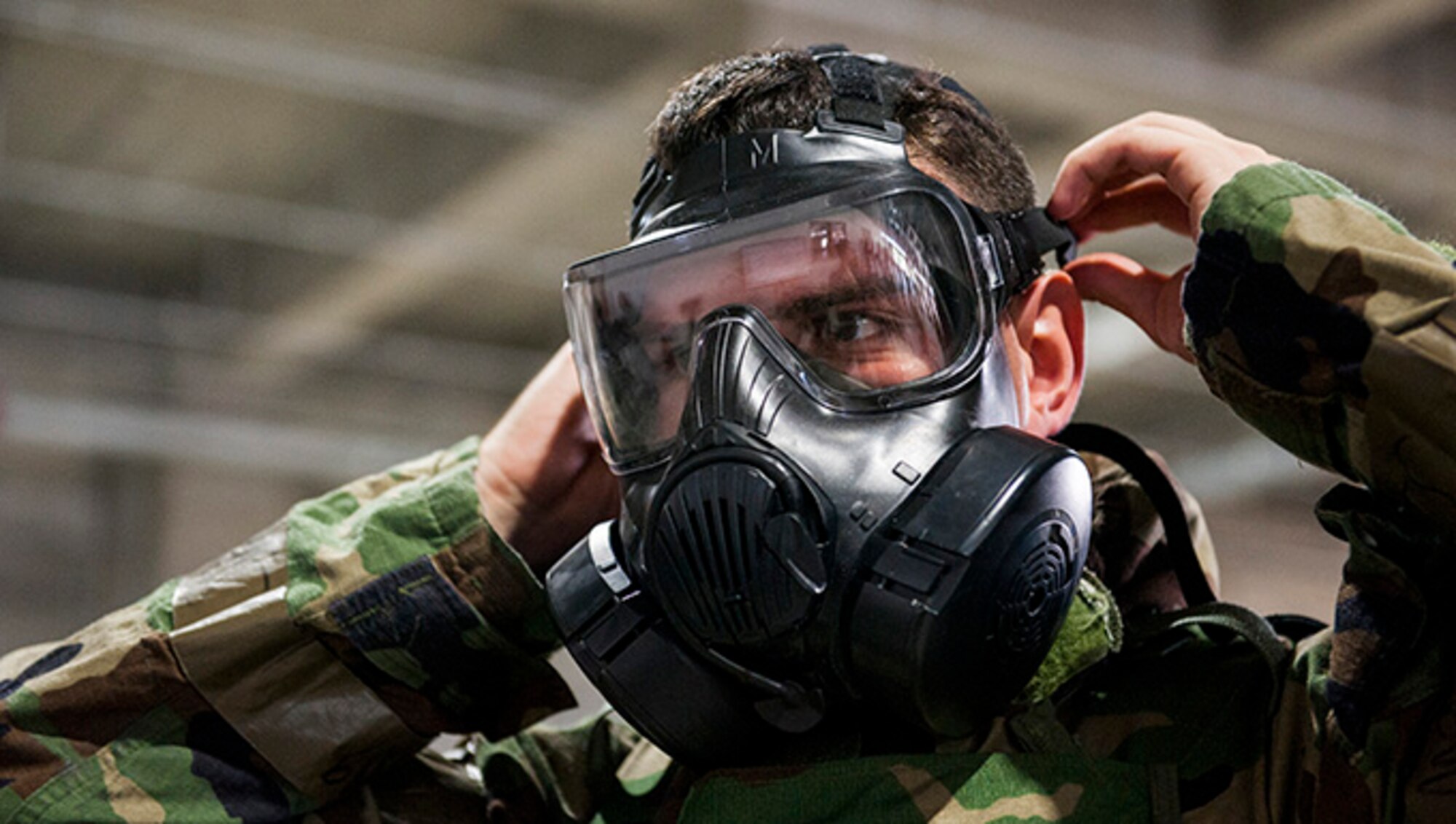 An Airman tightens his M50 gas mask while putting on his Mission Oriented Protective Posture gear during Ability to Survive and Operate training at Kadena Air Base, Japan, Sept. 12, 2019. The equipment is donned in the event of a chemical, biological, radiologic or nuclear threat. (U.S. Air Force photo by Naoto Anazawa)