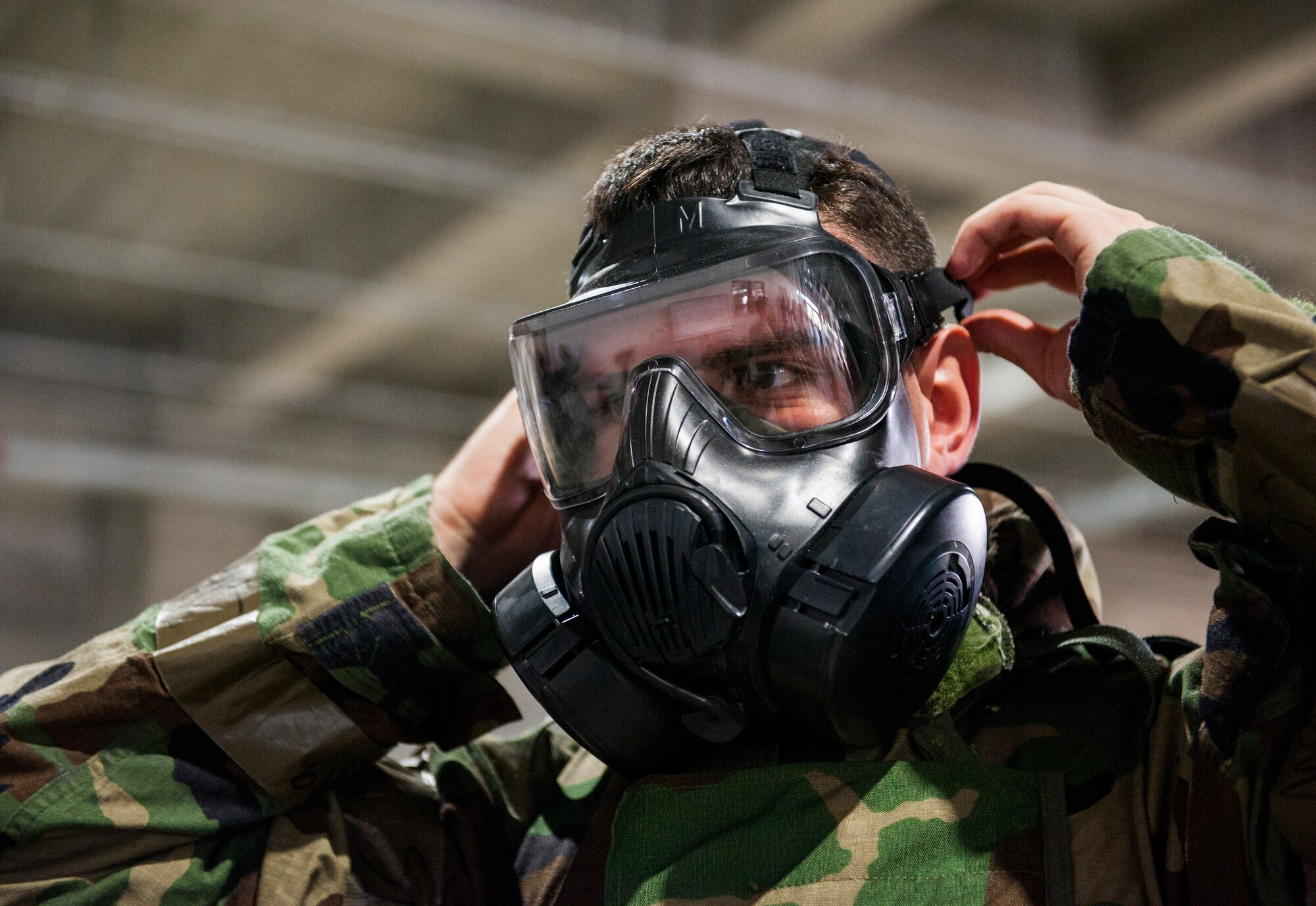 An Airman tightens his M50 gas mask while putting on his Mission Oriented Protective Posture gear during Ability to Survive and Operate training at Kadena Air Base, Japan, Sept. 12, 2019. The equipment is donned in the event of a chemical, biological, radiologic or nuclear threat. (U.S. Air Force photo by Naoto Anazawa)