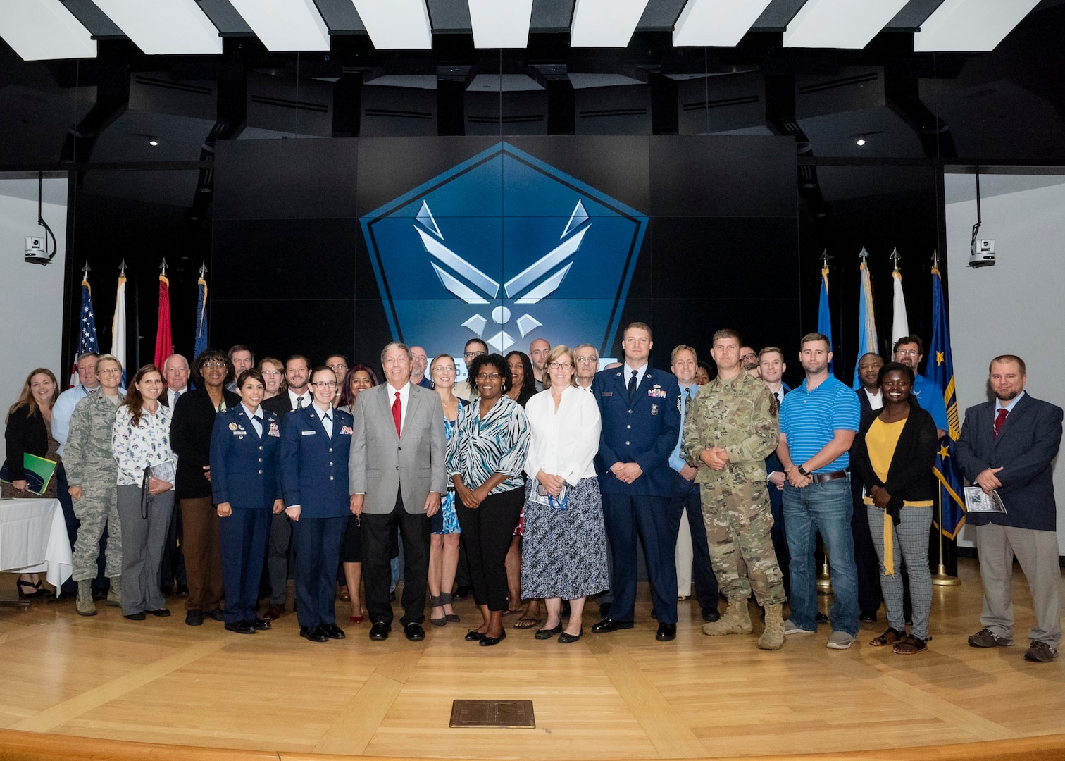 About 50 Air Force members pose for a group photo on a stage.