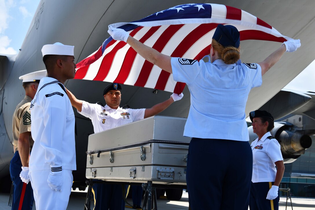 Service members raise a flag to drape a casket.