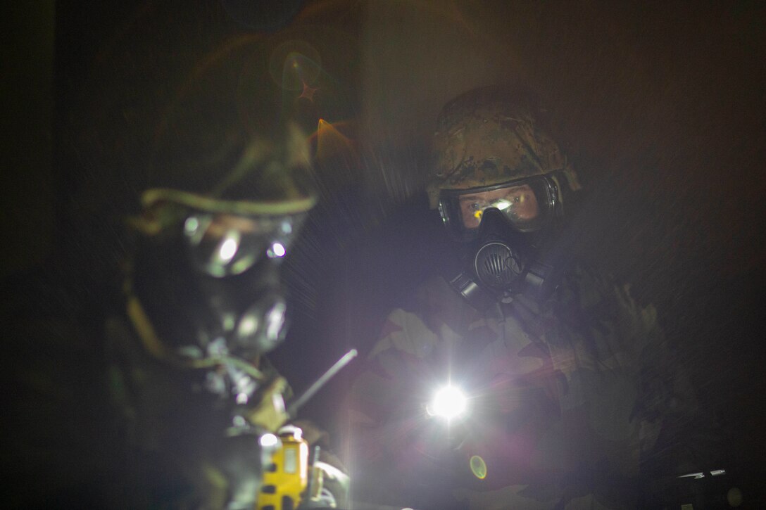 Two Marines read from a clipboard using a flashlight in the dark.