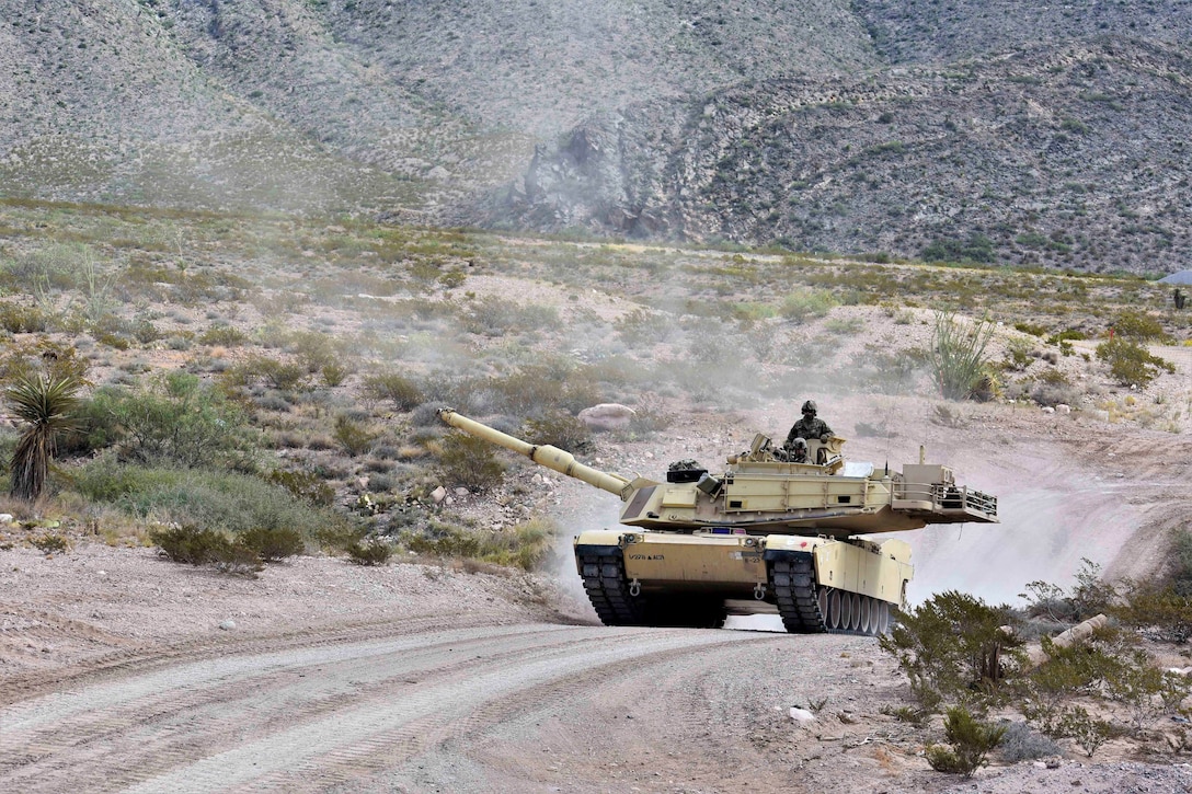 A soldier rides in a tank through the dessert.