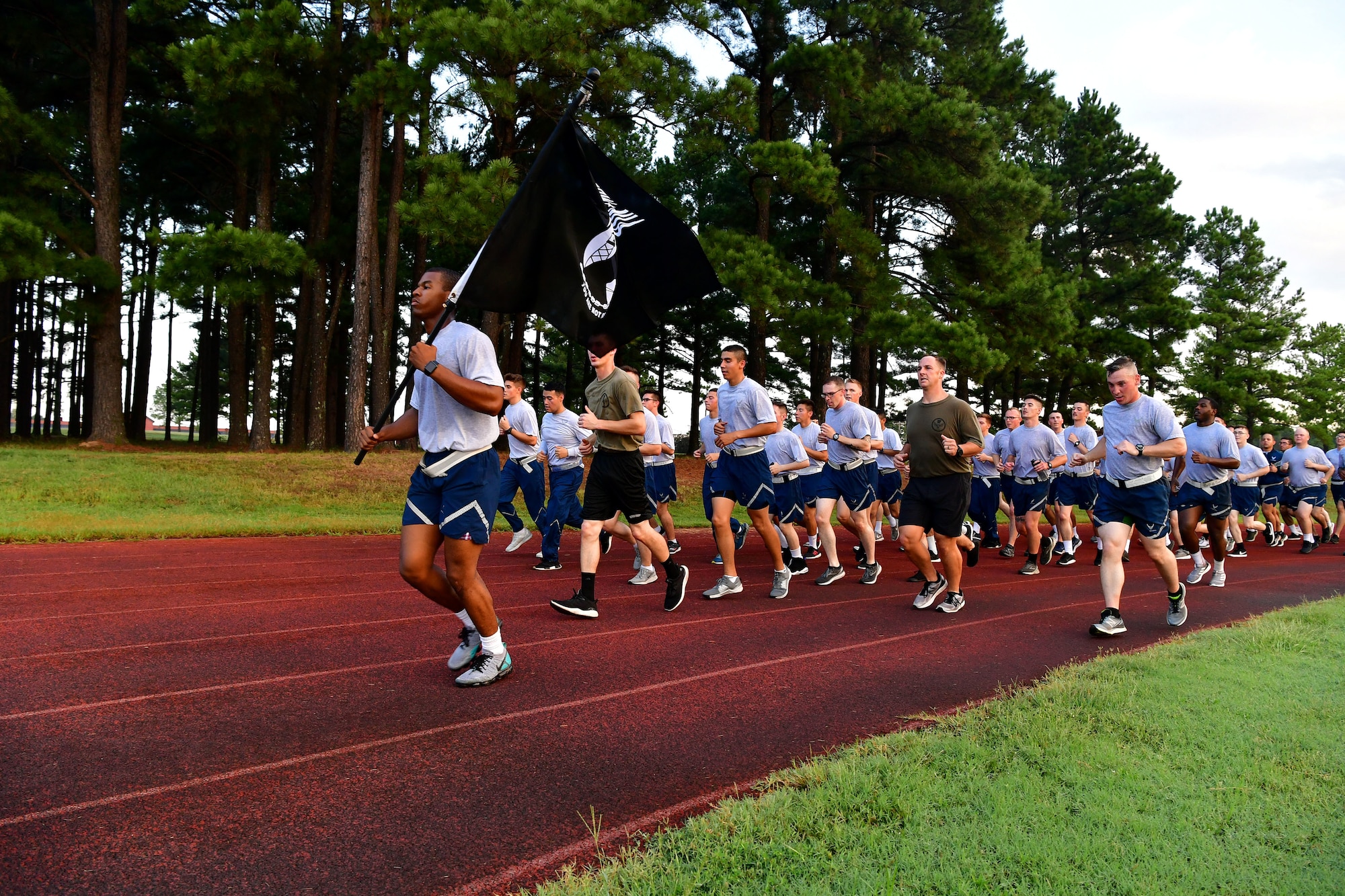 373rd training squadron run on the track in formation with a POW/MIA flag.