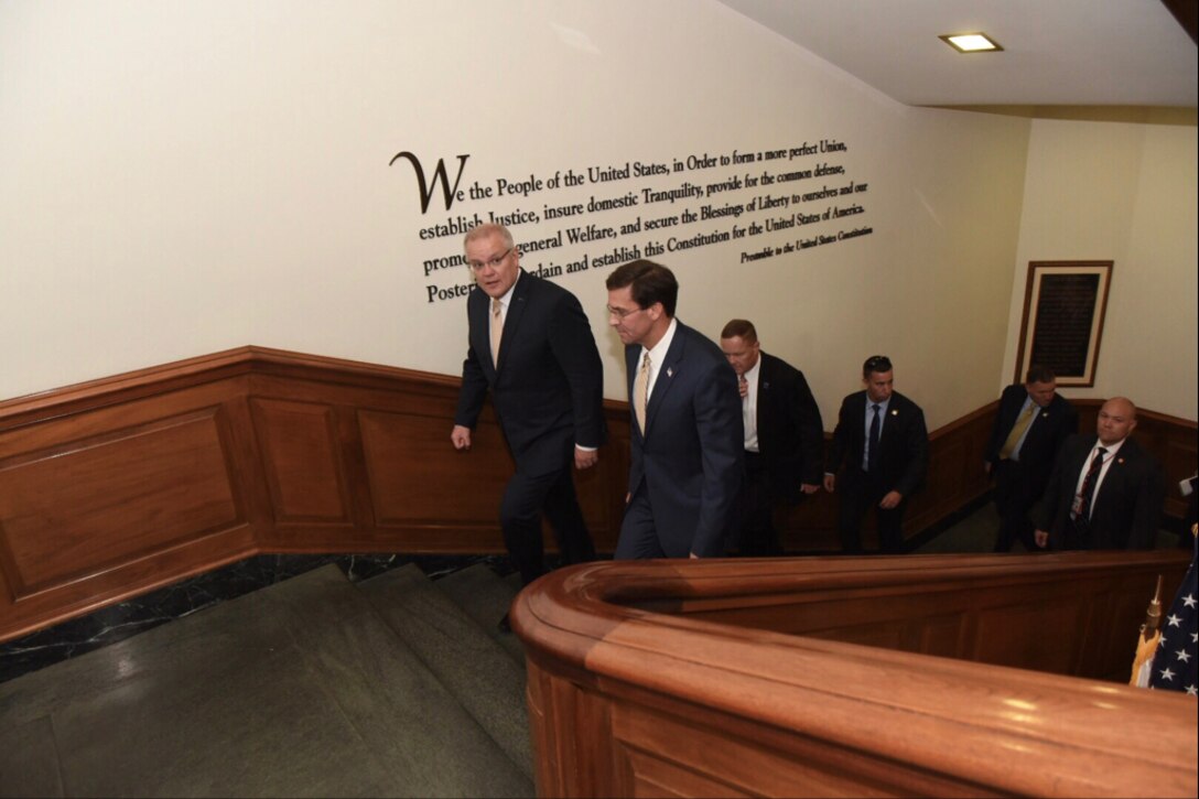 Men in suits walk up a staircase that has text from the preamble of the U.S. Constitution printed on one wall.