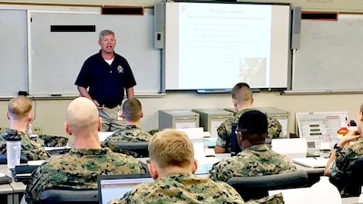 Classroom setting with instructor at the front and Marines seated in front of computers.