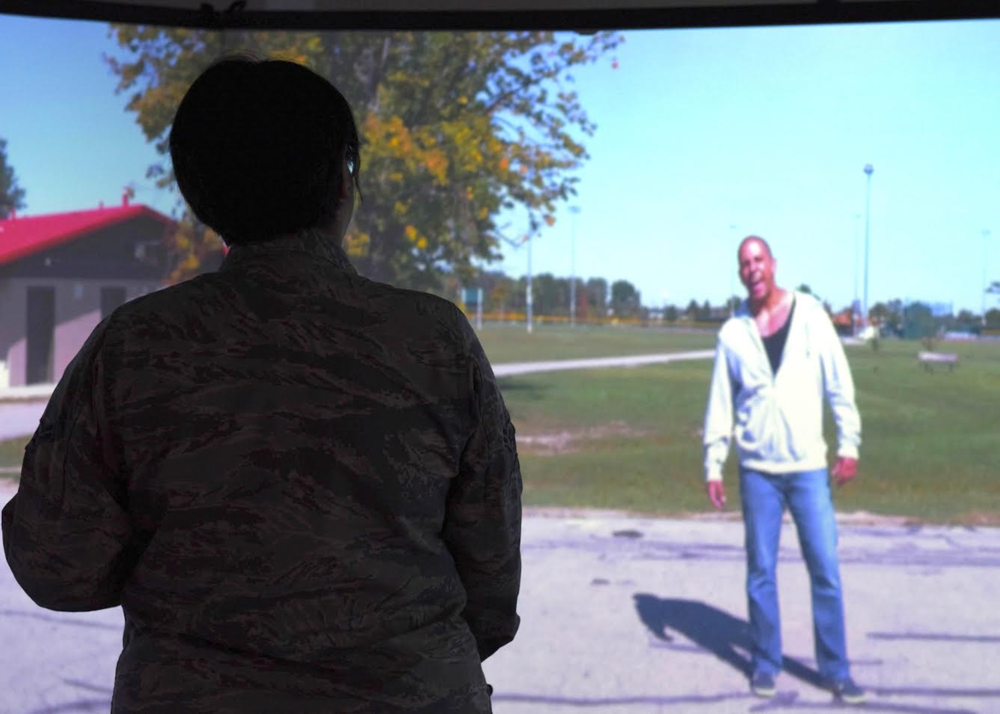 An Airman stands infront of a screen during a noise complaint simulation and tries to calm a male that is yelling.
