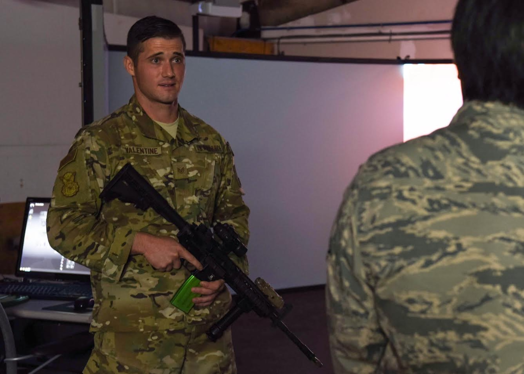 An instructor Airman holds an inert firearm as he briefs an Airman on how to use their simulation system.