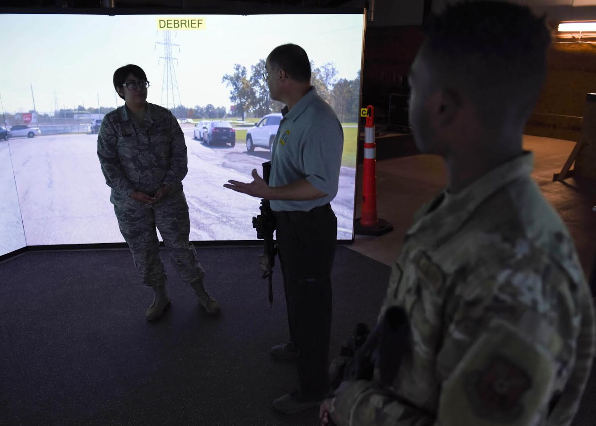 A civilian instructor stands between two Airmen during a debrief on a training simulation about a noise complaint.