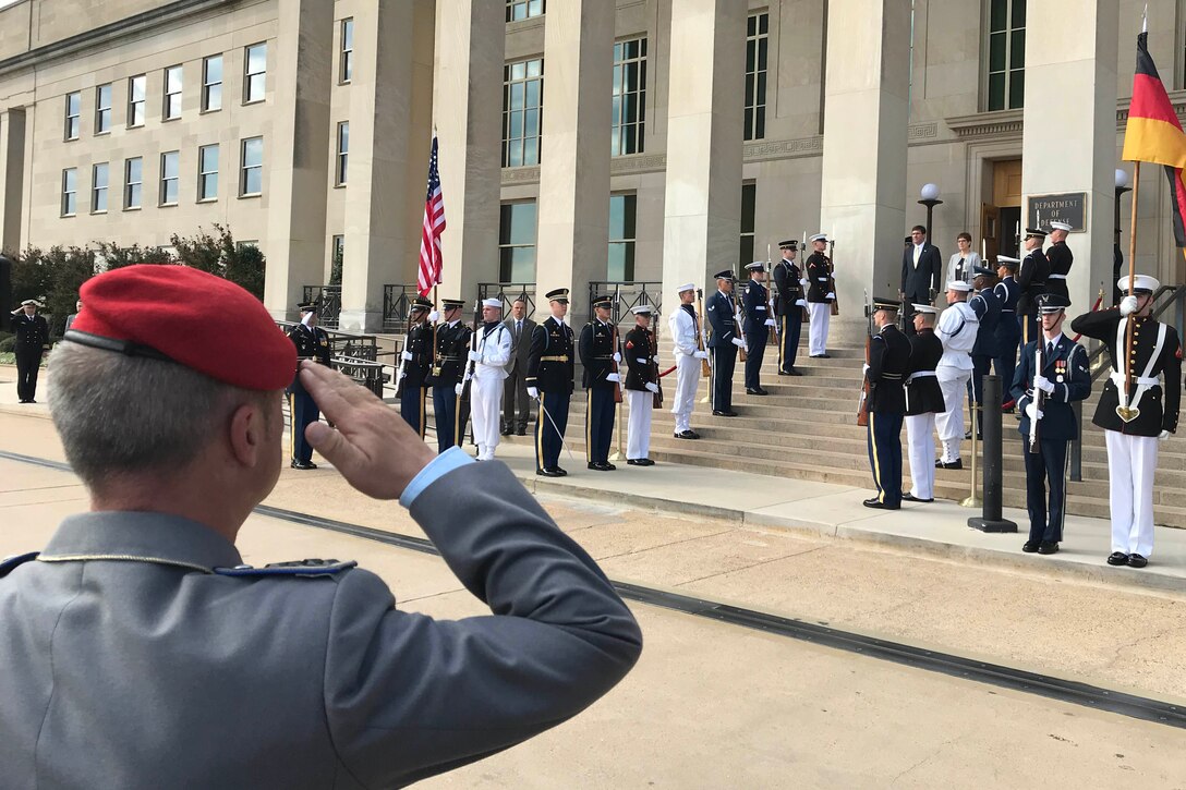 In the foreground, a German soldier salutes while a band plays and dignitaries stand at the Pentagon entrance.