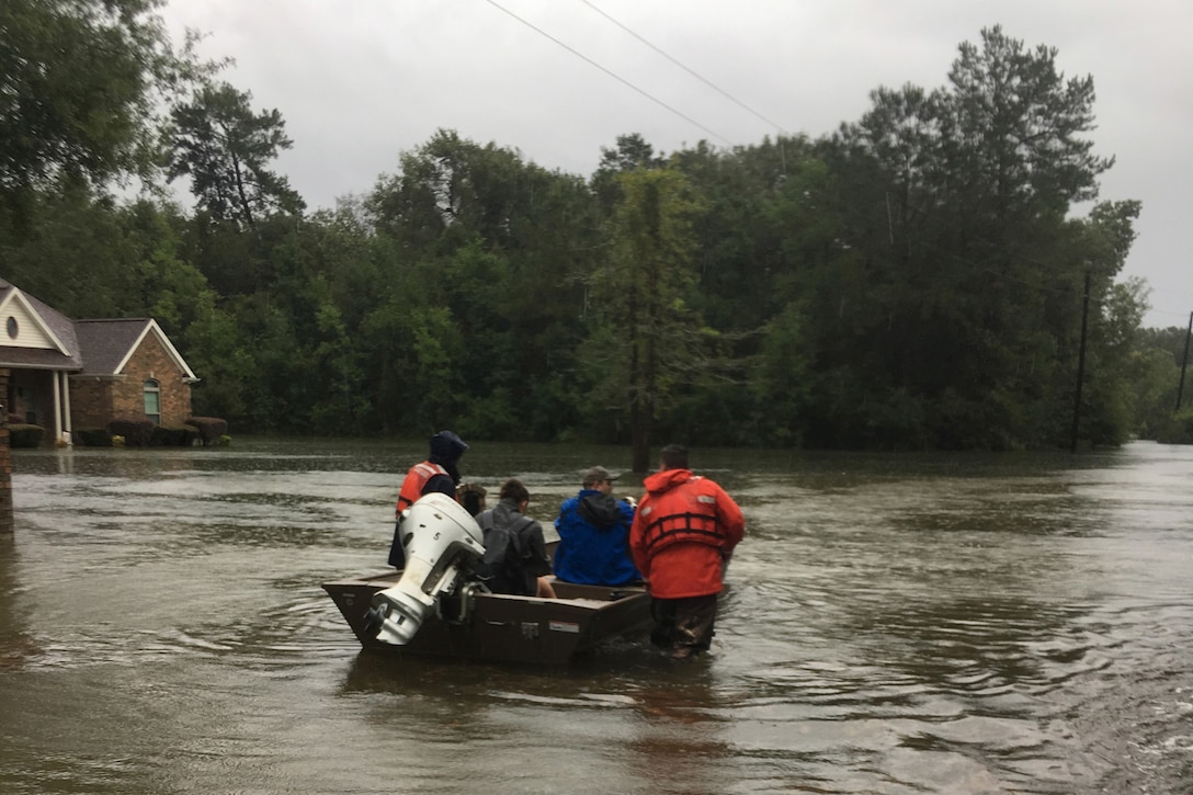 Coast Guardsman steer a boat carrying civilians in floodwaters.