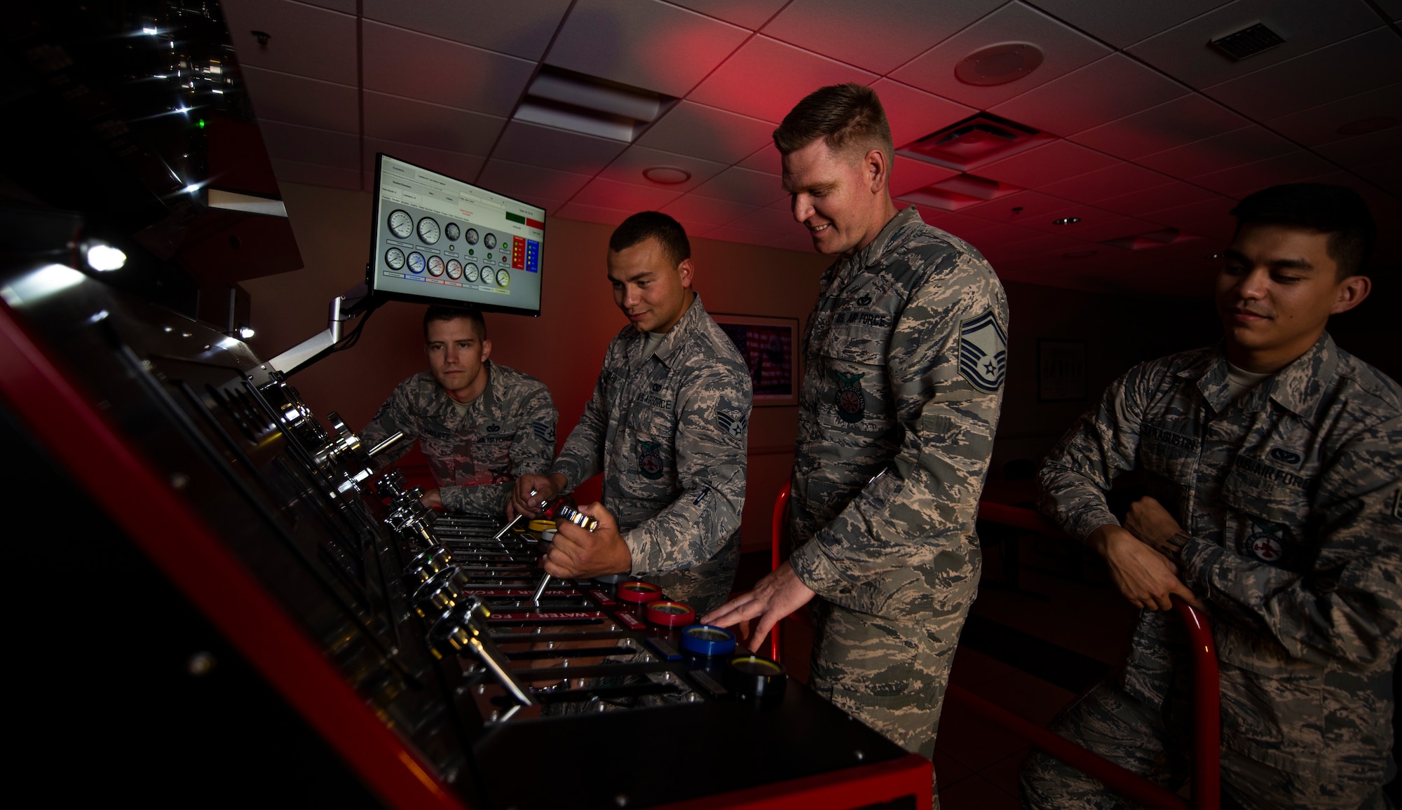 Four Airmen use a fire engine simulator for training.