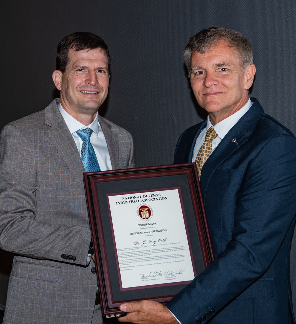 Dr. James “Tory” Cobb, distinguished scientist for advance signal processing and automation in mine warfare at Naval Surface Warfare Center Panama City Division, left, is presented with the National Defense Industrial Association (NDIA) Award for Technical Achievement in Undersea Warfare by Mike Cortese,division chair for the Undersea Warfare Division Sept. 17 in Groton, Connecticut.