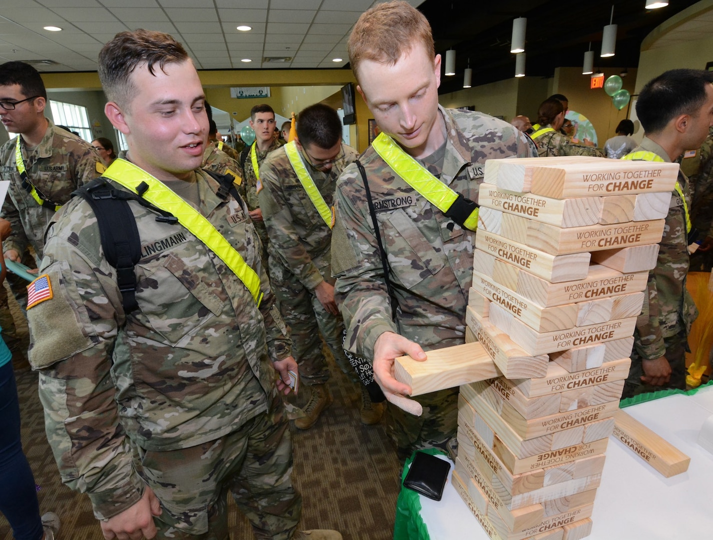 A Soldier slowly pulls out a wooden block from a tower labeled with “Together Working For Change.”
