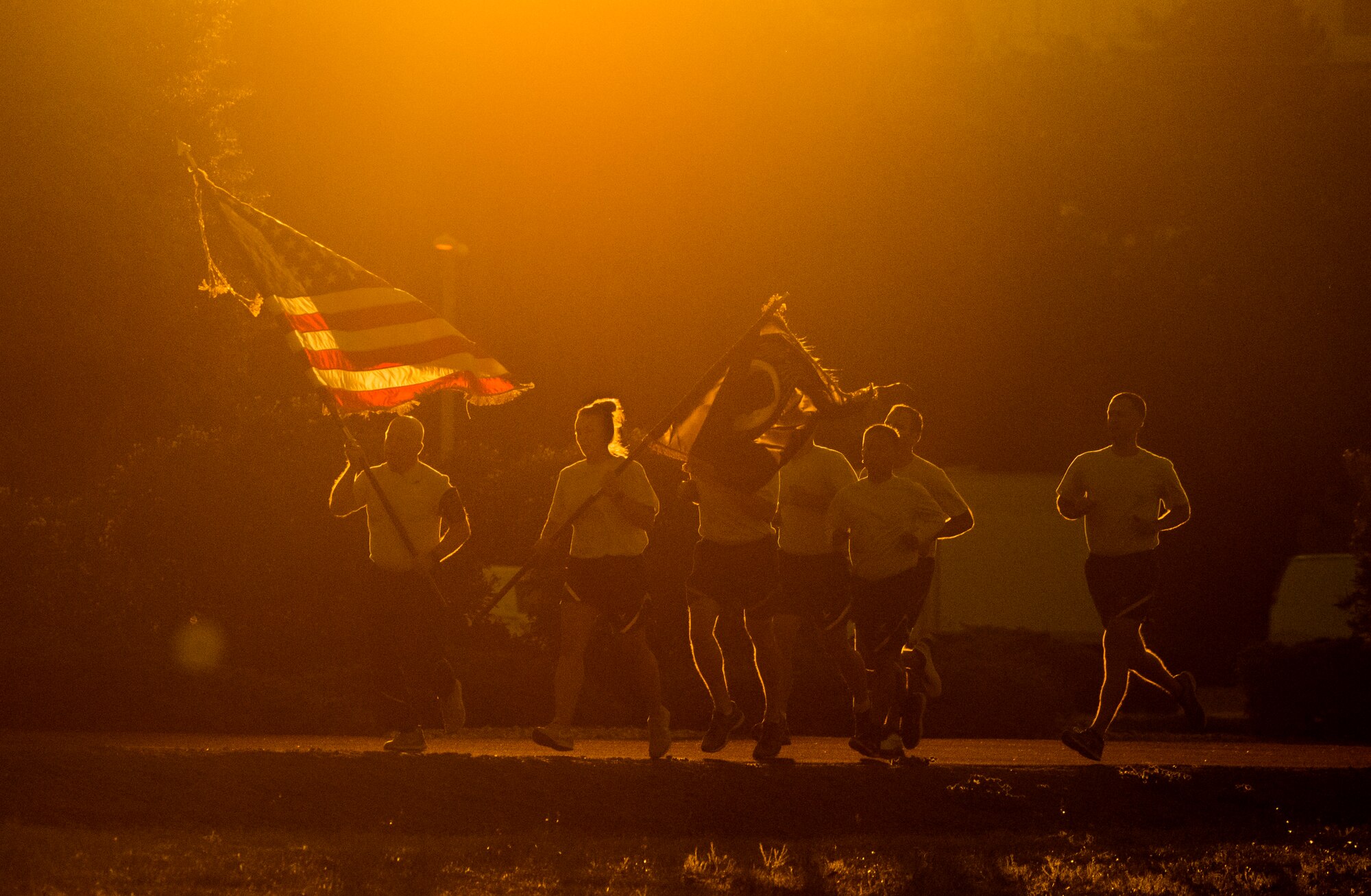 The sun rises as members of the 60th Air Mobility Wing Legal Office run on the fitness center track with the U.S. and POW/MIA flags Sept. 20, 2019, at Travis Air Force Base, California. Service members, civilians and family members kept the flags in constant motion for a 24-hour period. According to the Defense POW/MIA Accounting Agency, more than 82,000 Americans remain missing from WWII, Korean War, Vietnam War, Cold War, Gulf Wars and other conflicts. The names of service members still unaccounted for were recited throughout the run. (U.S. Air Force photo by Heide Couch)