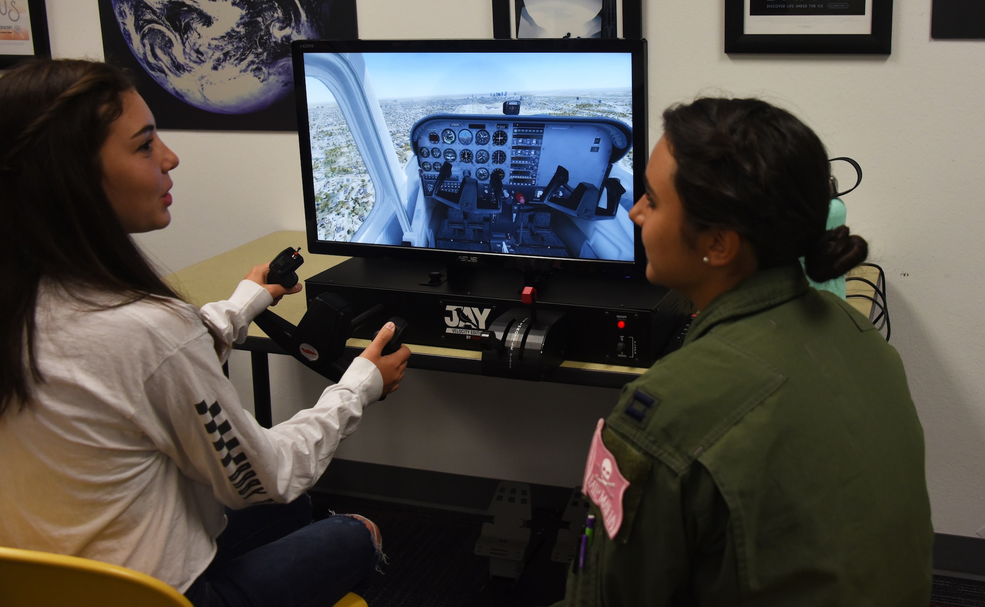 An Air Education and Training Command Women’s Fly-In Event participant guides a young woman through a flight simulator at the Girls in Aviation Day