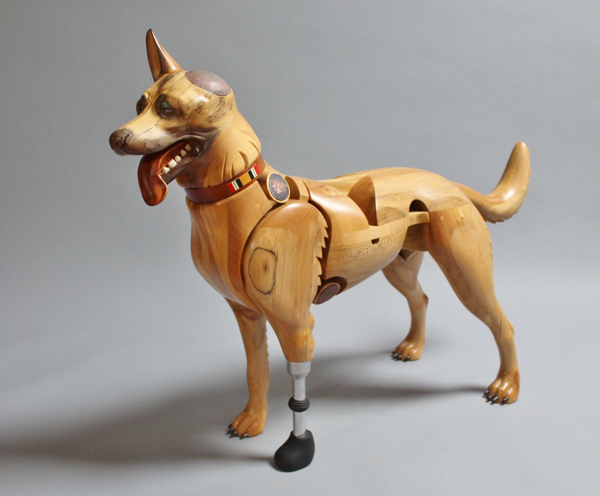 Picture of a wood sculpture dog who is missing an ear and has a prosthetic leg.