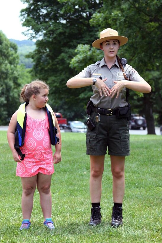 A Park Ranger demonstrates the proper way to wear a life jacket to a child during an event.