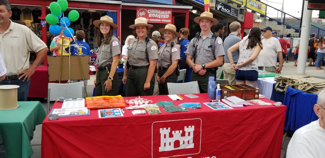 Four Park Rangers pose at an exhibit table with water safety materials during an event.