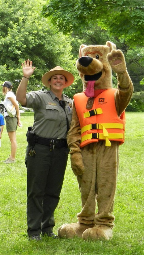 A Park Ranger and Bobber the Water Safety Dog Mascot wave to the camera during an event.
