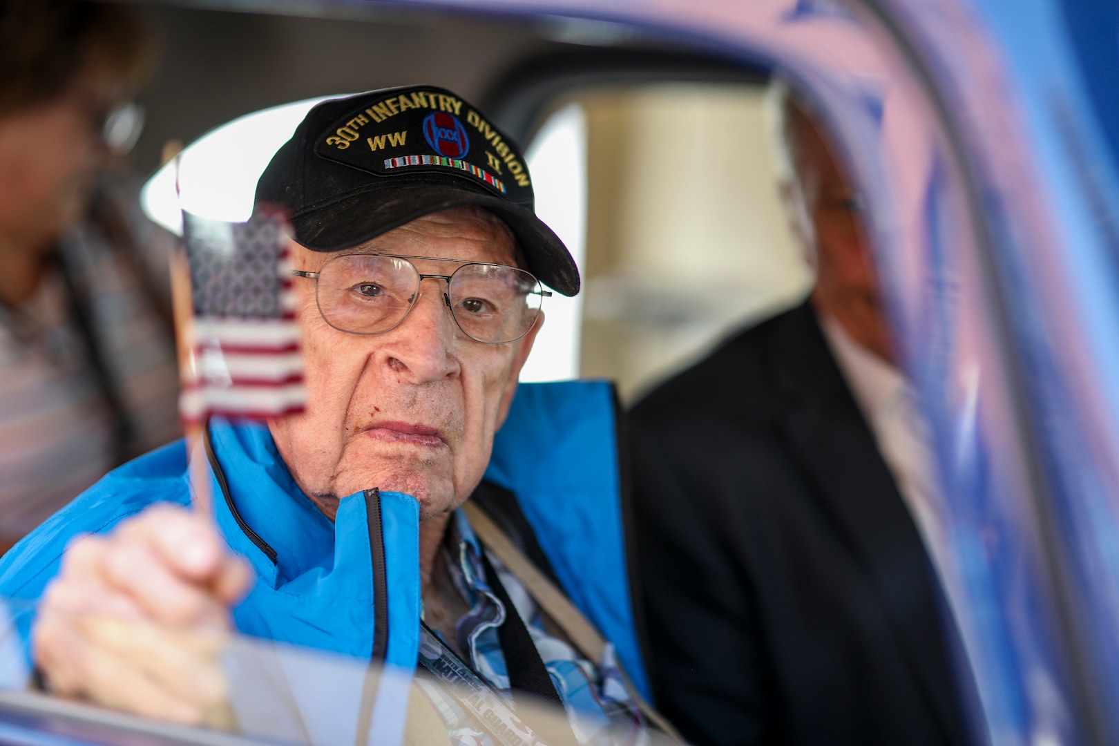 George Hamm, a WWII veteran who served with the 30th Infantry Division,  holds a flag out a window during a parade through Maastricht in the Limburg Province of the Netherlands tSept. 14, 2019, in celebration of the 75th anniversary of the liberation by 30th Infantry Division Soldiers in September 1944. North Carolina National Guard Soldiers escorted the veterans, with whom they share a unit lineage, riding in classic cars and WWII era military vehicles through the streets lined with thousands of people.