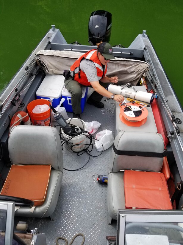 A Park Ranger riding on a boat collects a water sample for testing and monitoring purposes.