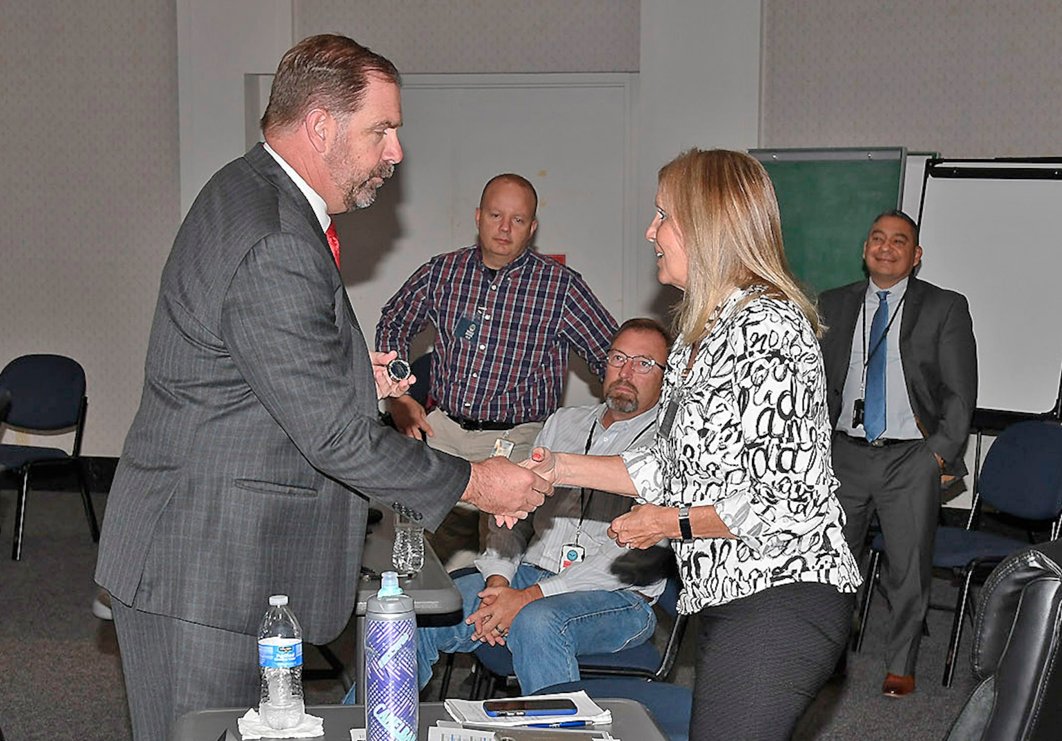 DLA Disposition Services Director Mike Cannon "coins" GSA Southwest Central Branch Chief Ericka Grim during a combined DLA-GSA sales contracting officer training event.