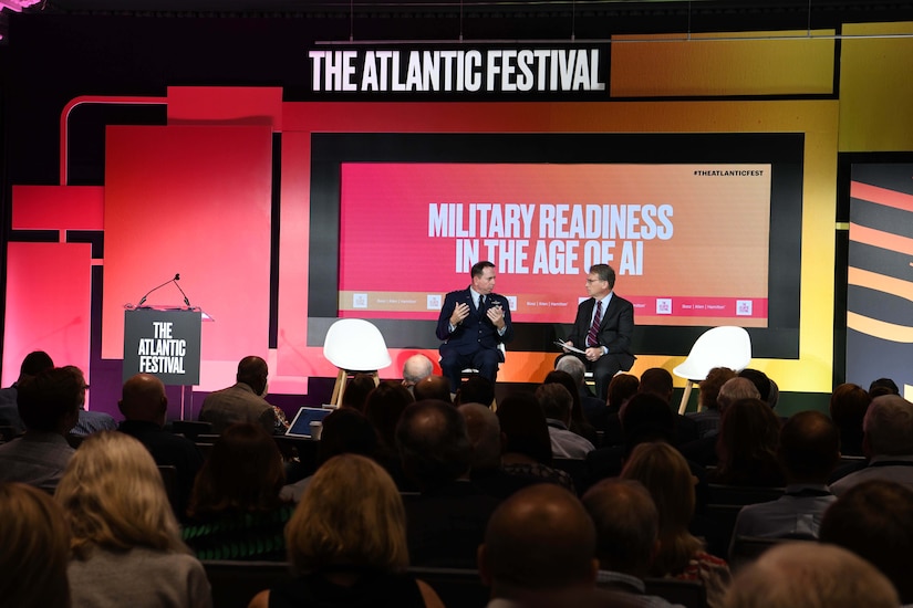 View from audience of two men on a stage talking. Above them, signs read, “The Atlantic Festival” and “Military Readiness in the Age of AI.”