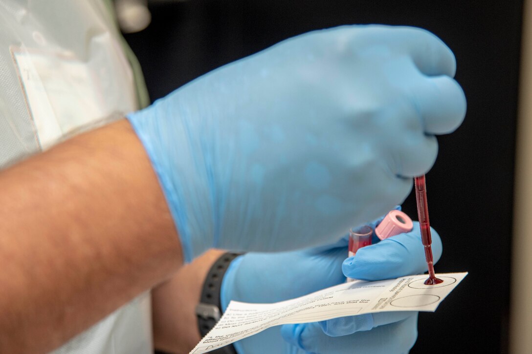 A gloved hand squirts blood onto a paper card.