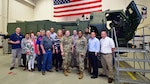 A group of people stand in front of a Multiple Launch Rocket System launcher unit.