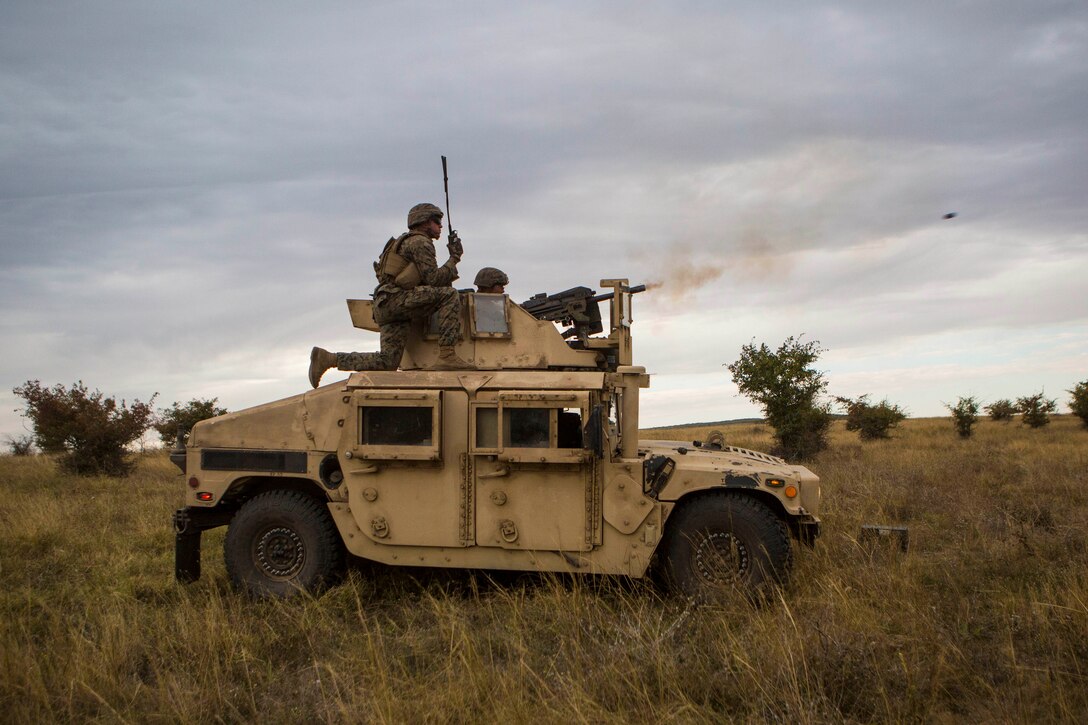 A Marine fires a weapon from the top of a military vehicle.