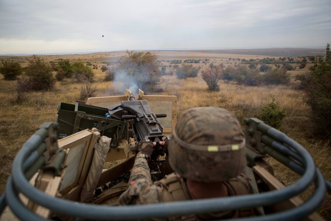 A Marine fires a weapon form the top of a military vehicle.