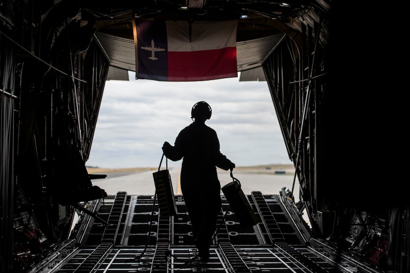An airman walks inside an aircraft holding two blocks.
