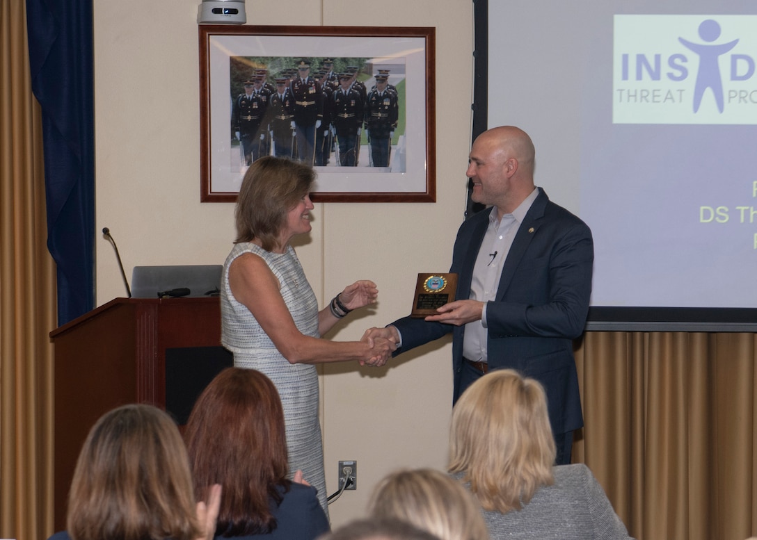 Woman presents man with a DLA plaque.