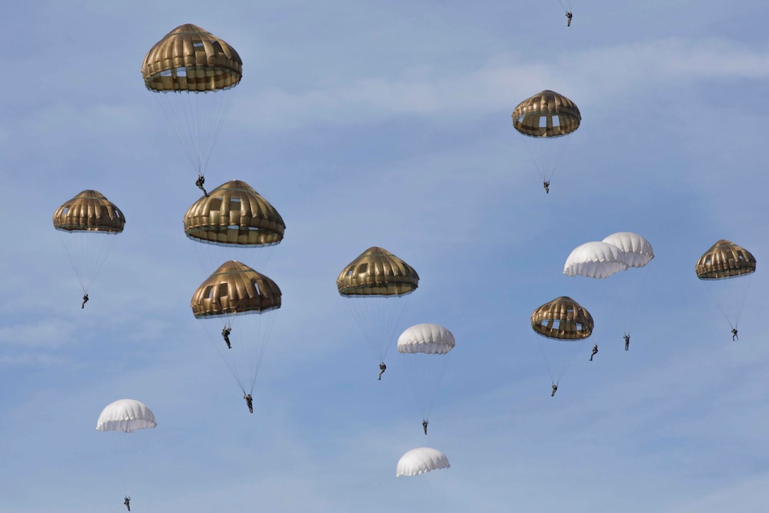 A large group of paratroops parachute in the sky.