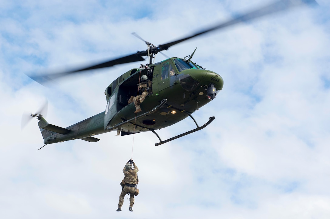 An airman is hoisted up towards a helicopter by another airman.