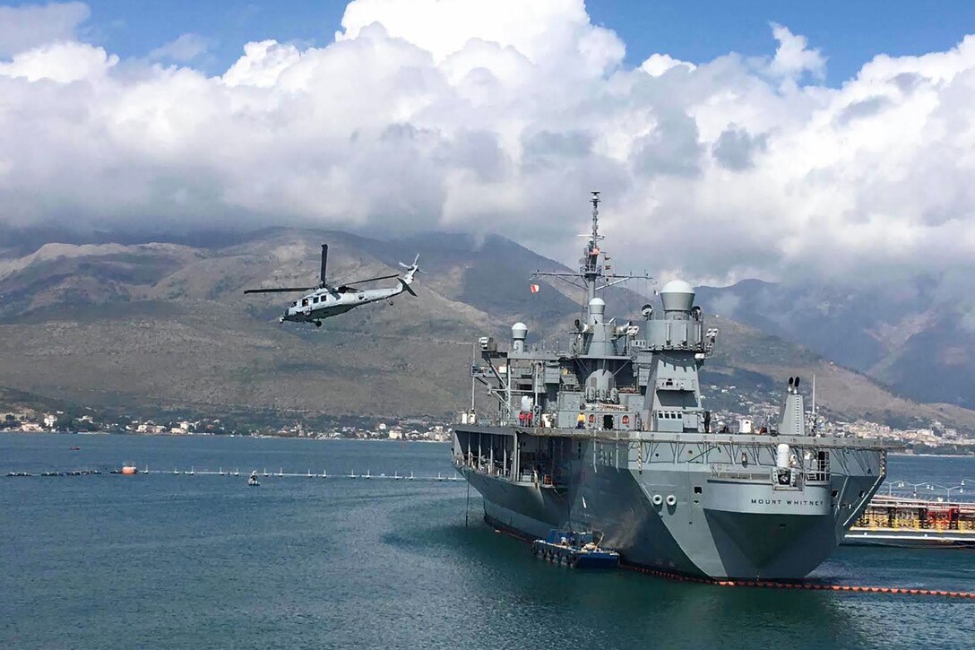 A helicopter flies above a ship at a port.