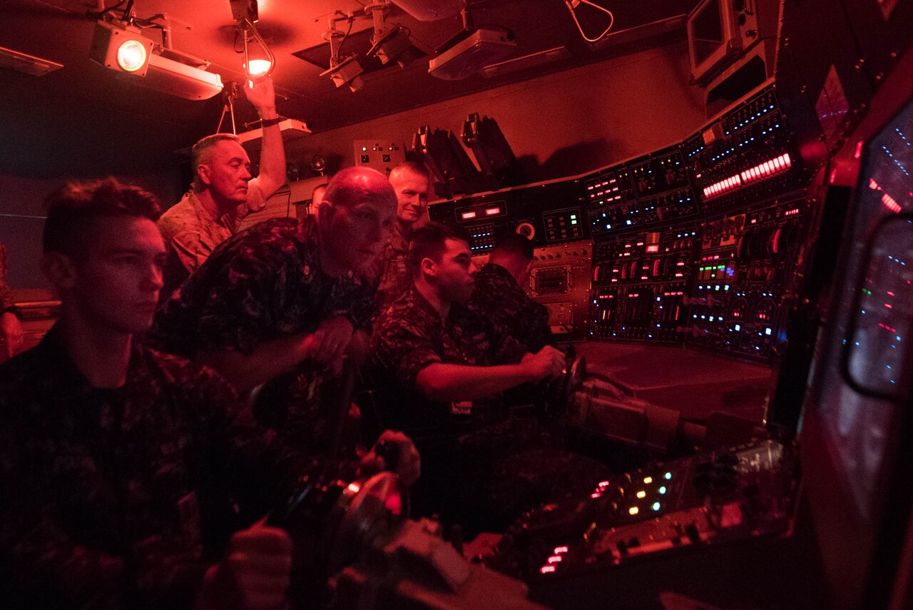 Service members watch sailors drive a submarine.
